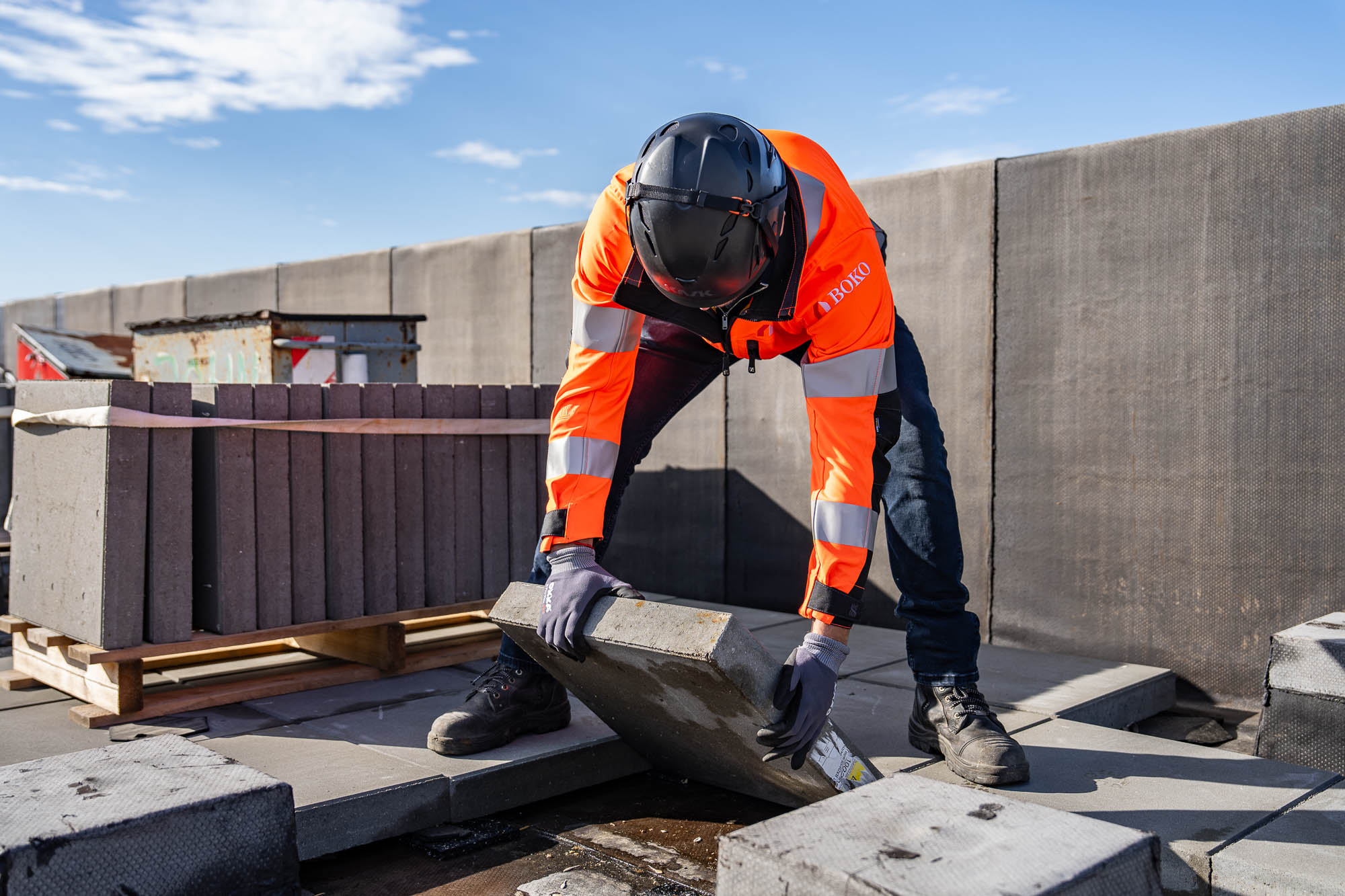 Een medewerker van BOKO Dakbedekkers tilt een betonnen tegel op het dak van de Dreeftoren in Amsterdam.
