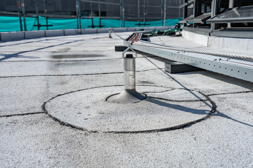 Ankerpunt met staalkabel voor valbeveiliging, ingewerkt in de witte dakbedekking van JinSo in Amsterdam.